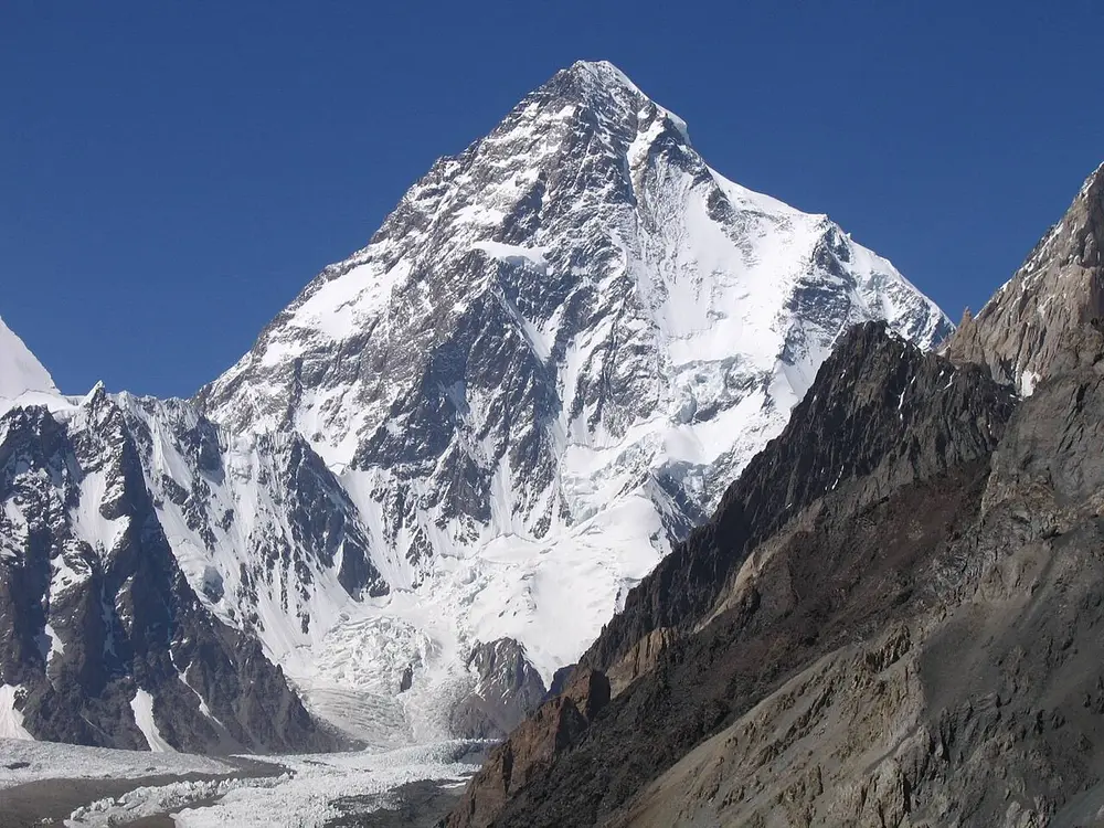 A huge pyramid-shaped snowy mountain above a glacier, with dark rock ridges in front.