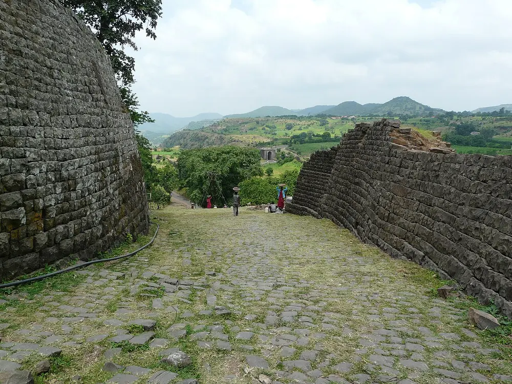 An old stone gateway and walls on a plateau edge, with green hills in the distance.