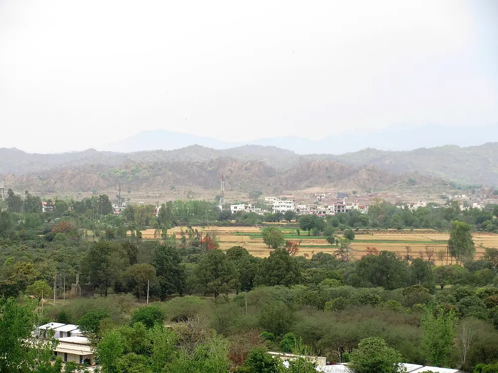 Low, dry, rugged hills on the horizon beyond green fields and trees.
