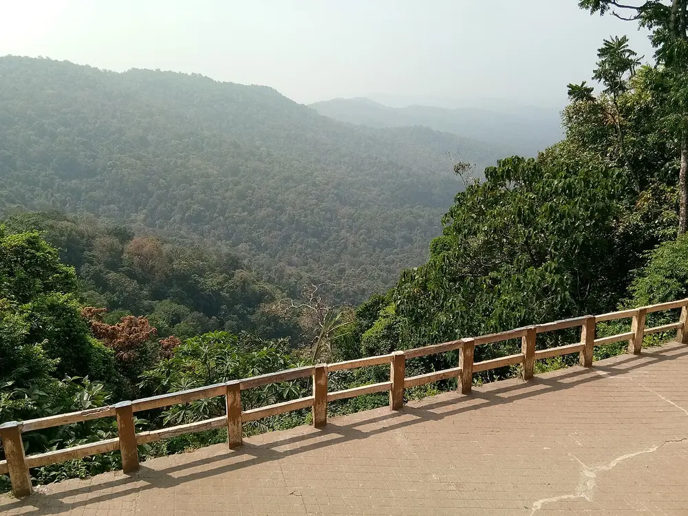 A view from a railed viewpoint over steep hills covered in green forest, fading into haze.