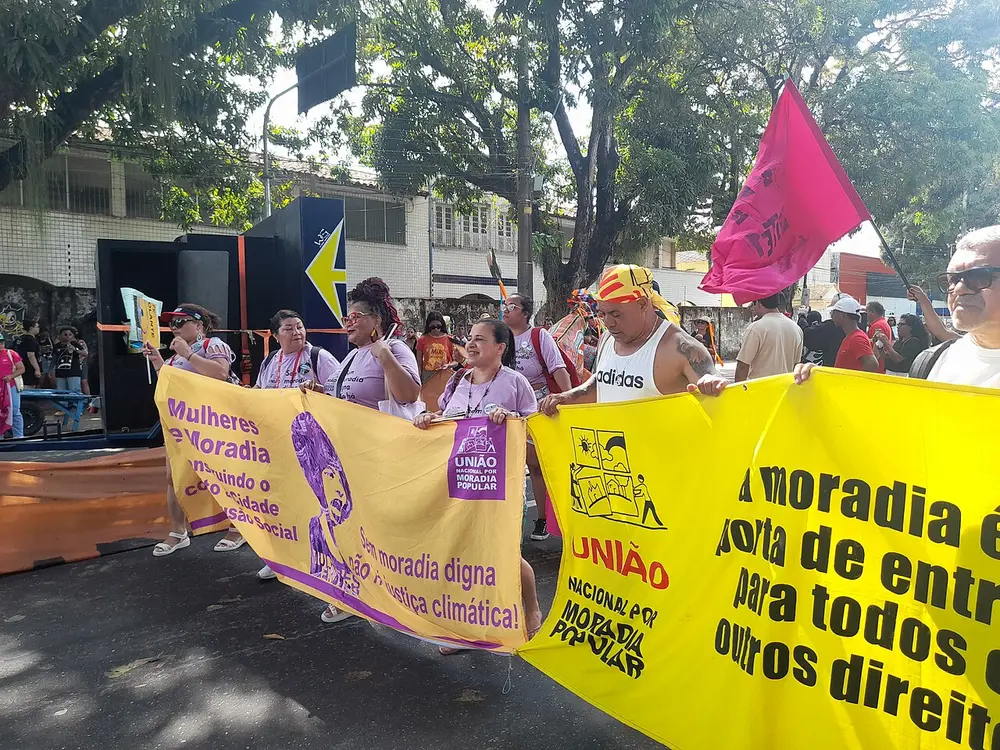 Marchers carry large yellow banners and a pink flag along a tree-lined street in Belém during a climate march.