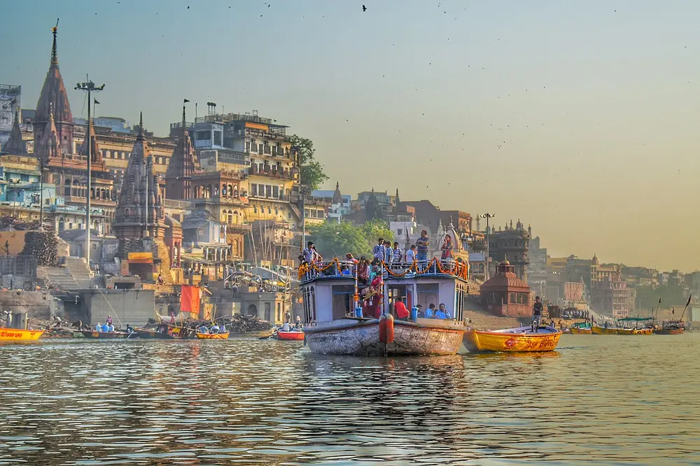 The Ganga at Dashashwamedh Ghat in Varanasi at dawn, with crowded boats on the water and old temples and houses along the steps of the riverbank.