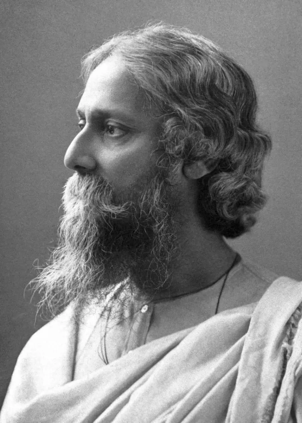 A black and white portrait of Rabindranath Tagore in profile, with long wavy grey hair and a full beard, wearing a shawl.