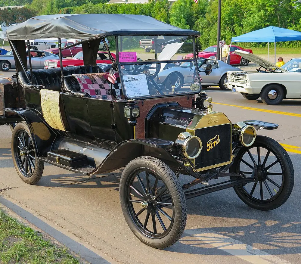 A black 1914 Ford Model T touring car with its fabric roof up, large round headlamps, thin spoked wheels and the Ford name on its radiator, parked at an outdoor car show.