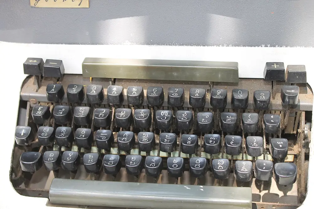 Close-up of the keyboard of an old grey Godrej typewriter, with Kannada letters on its rounded black keys and part of a Godrej name plate at the top.