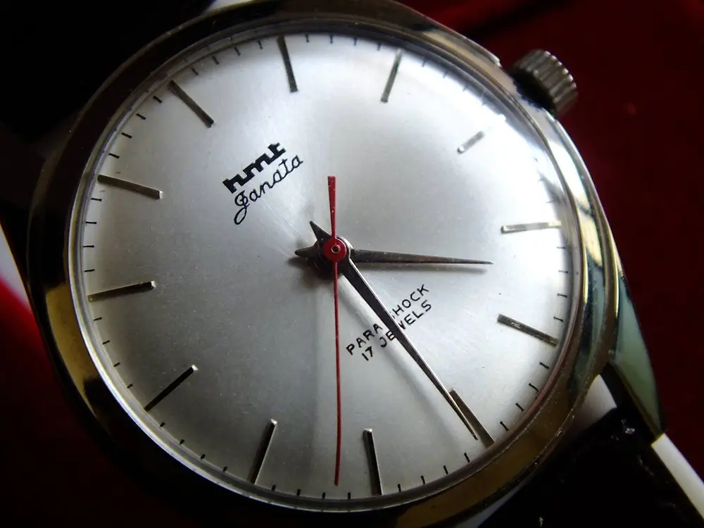 Close-up of an HMT Janata wristwatch with a plain silver dial, thin line markers instead of numbers, a red seconds hand and the words HMT Janata near the top.