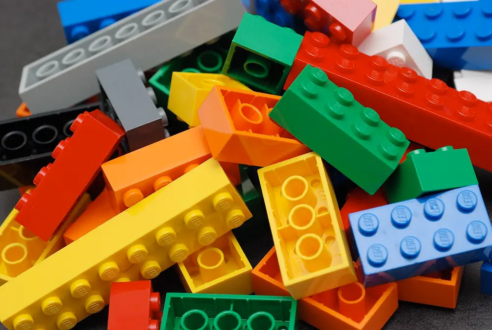A heap of Lego bricks in red, yellow, green, blue, orange and grey, of different lengths, with the round studs on their tops showing.