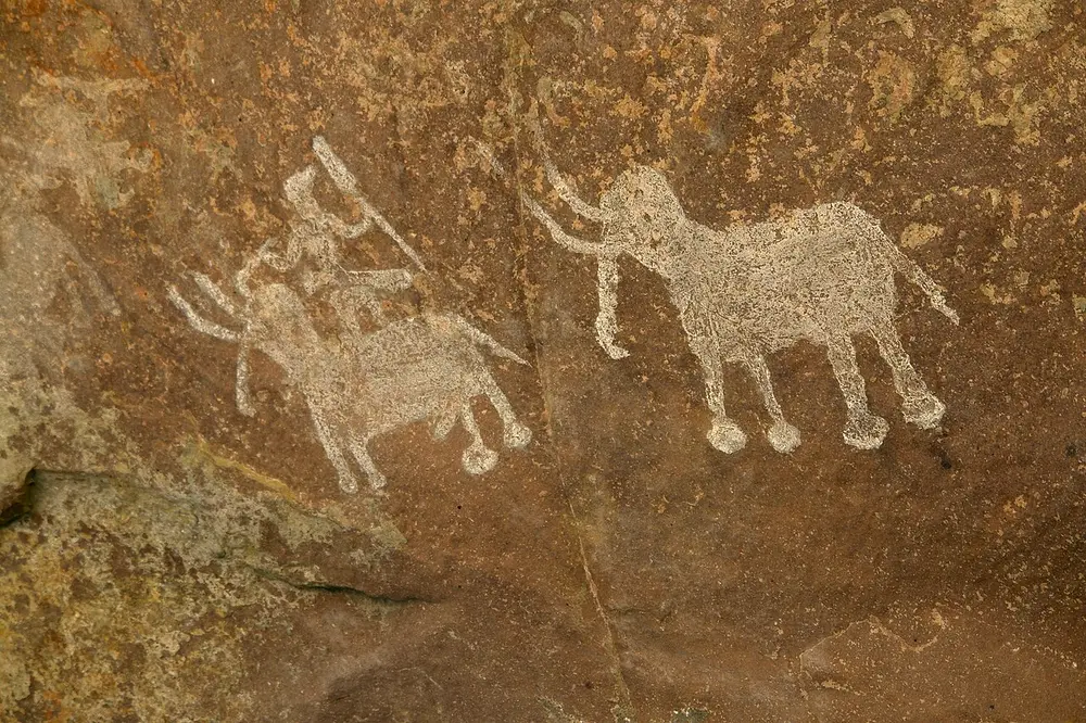 Two white elephants painted on a brown rock, one carrying a rider holding a long spear or goad.