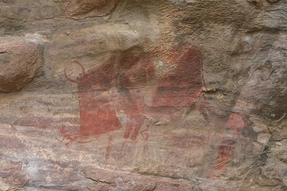 A huge red animal with horns and a spiky back fills a rock wall, while a tiny red stick figure of a man runs in front of it.