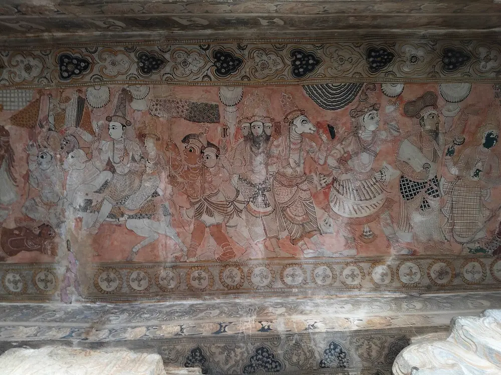A long ceiling painting on a red ground showing a row of gods and attendants in patterned clothes, with faces in profile and large eyes, between bands of flower patterns.