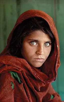 A portrait of a young girl with striking green eyes and a red headscarf, looking straight at the camera.