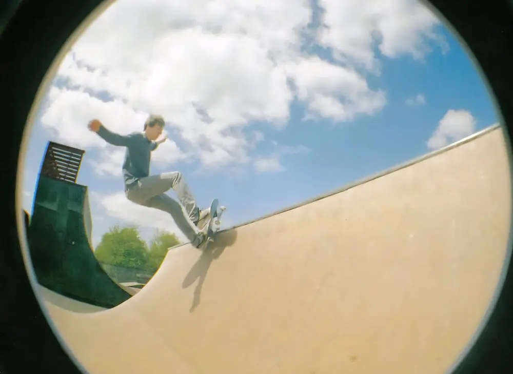 A round, bowl-shaped photo of a skateboarder in the air above a curved concrete ramp, with blue sky and clouds, and the edges of the picture bending in a circle.