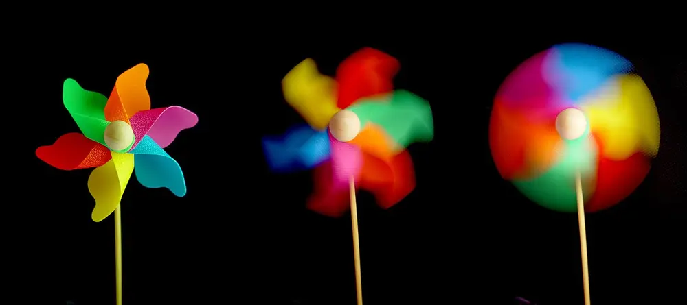Three photos of the same colourful paper pinwheel on a stick against a black background. On the left its blades are sharp; in the middle they are a little blurred; on the right they have melted into a smooth circle of colour.