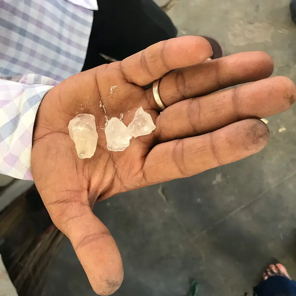 An open palm holding three small clear crystals of alum.