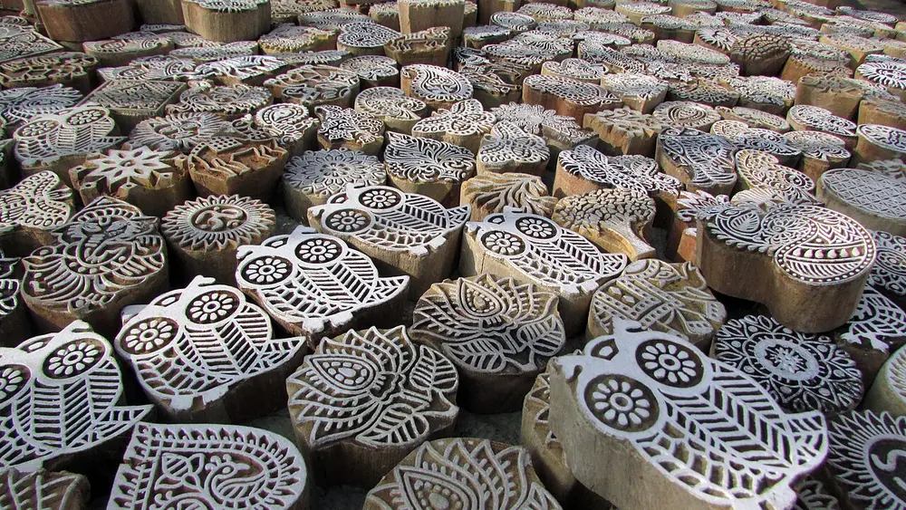 Hundreds of carved wooden printing blocks piled together, their faces cut with paisleys, flowers and leaves.