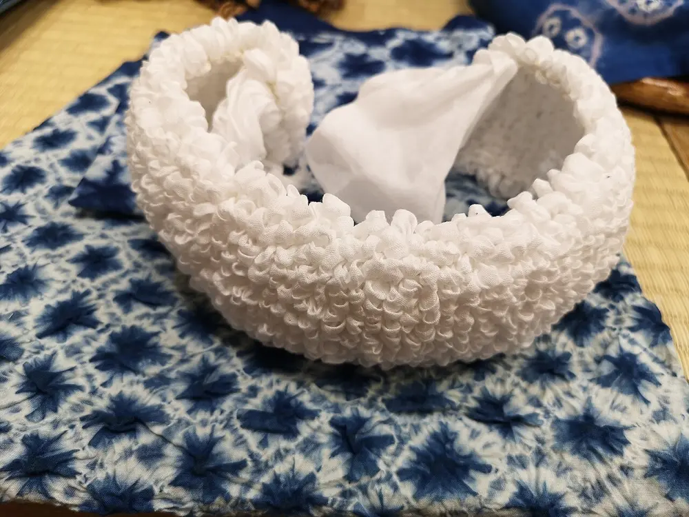 A piece of white cloth still bound up in tight little puckers, sitting on a finished indigo cloth patterned with white star-like spots.