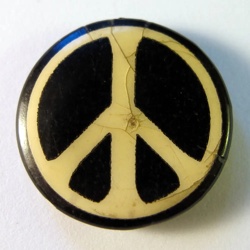 An old round cream badge with a black circle and, inside it, a cream upright line with two lines sloping down from its centre, leaving four black wedges.