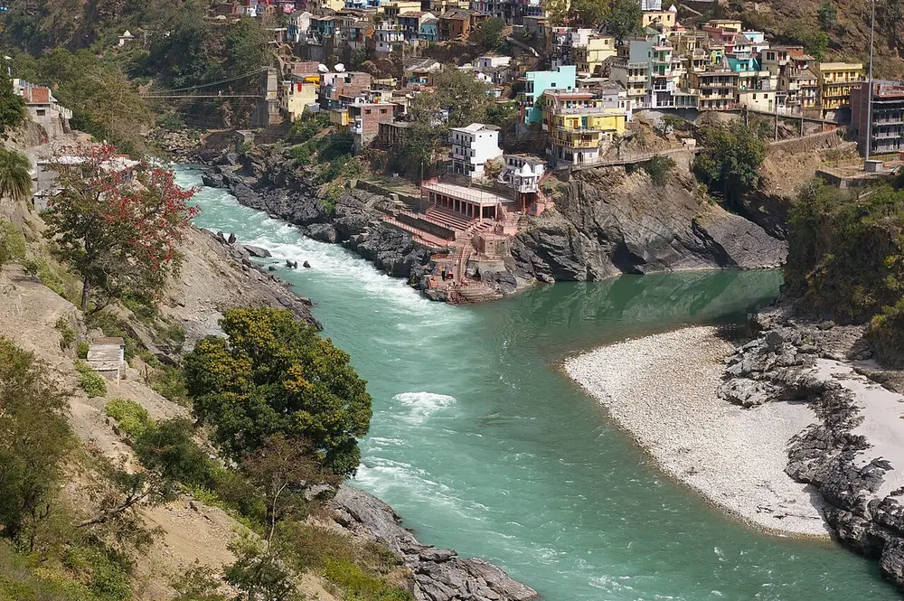 Two rivers meeting in a steep green gorge below a hillside town, one rushing and clear green, the other calmer.