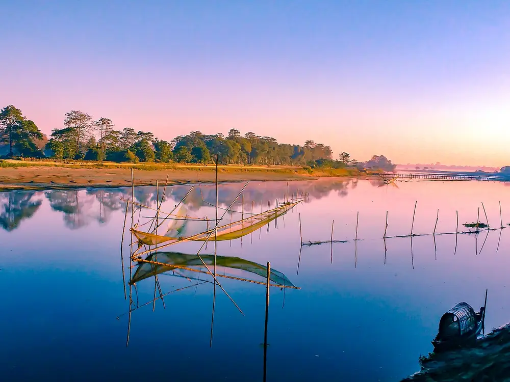 A still river reflecting a pink and blue dawn sky, with bamboo fishing nets standing in the water.