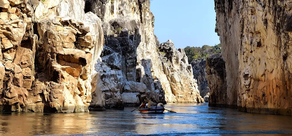 A calm river running between tall white and cream cliffs of marble, with small boats on the water.