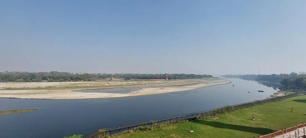 A wide, slow river with sandbanks, seen from a high stone terrace with a lawn and railing.