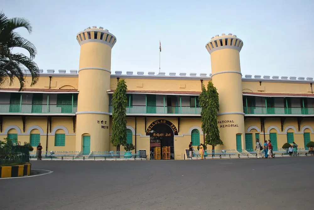 A cream and green colonial prison building with two round towers flanking its entrance, under a blue sky.