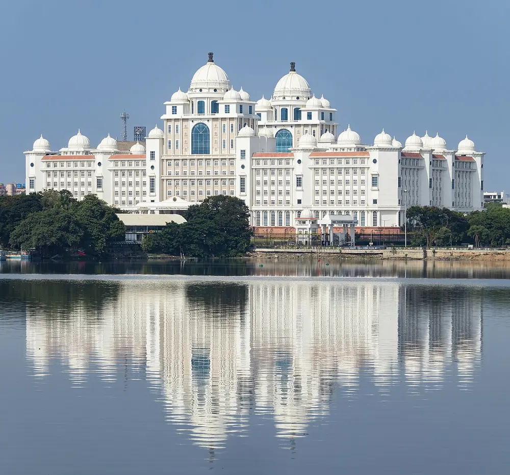 A huge white government building with many domes, reflected in a still lake.