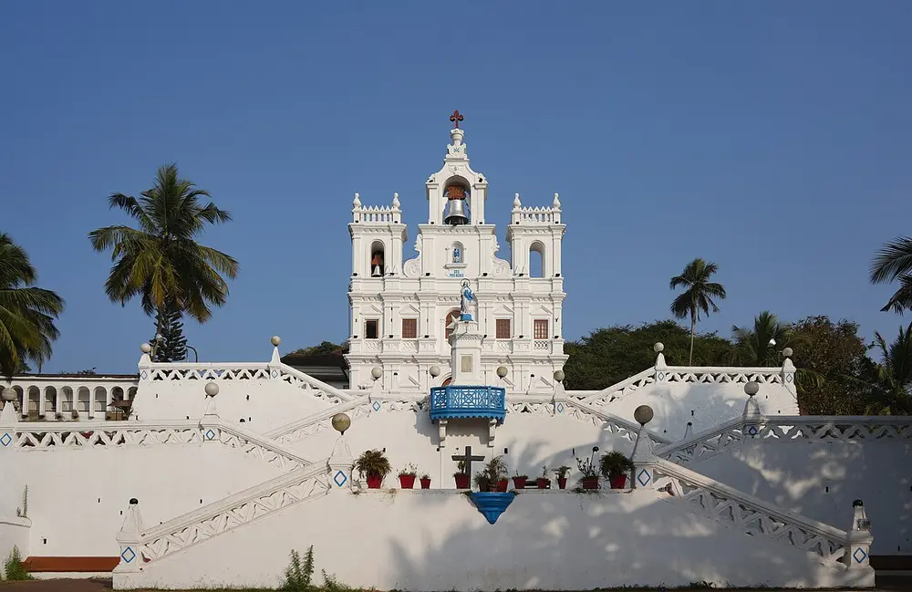 A white church with a tall bell tower at the top of a zigzag stairway, against a deep blue sky.