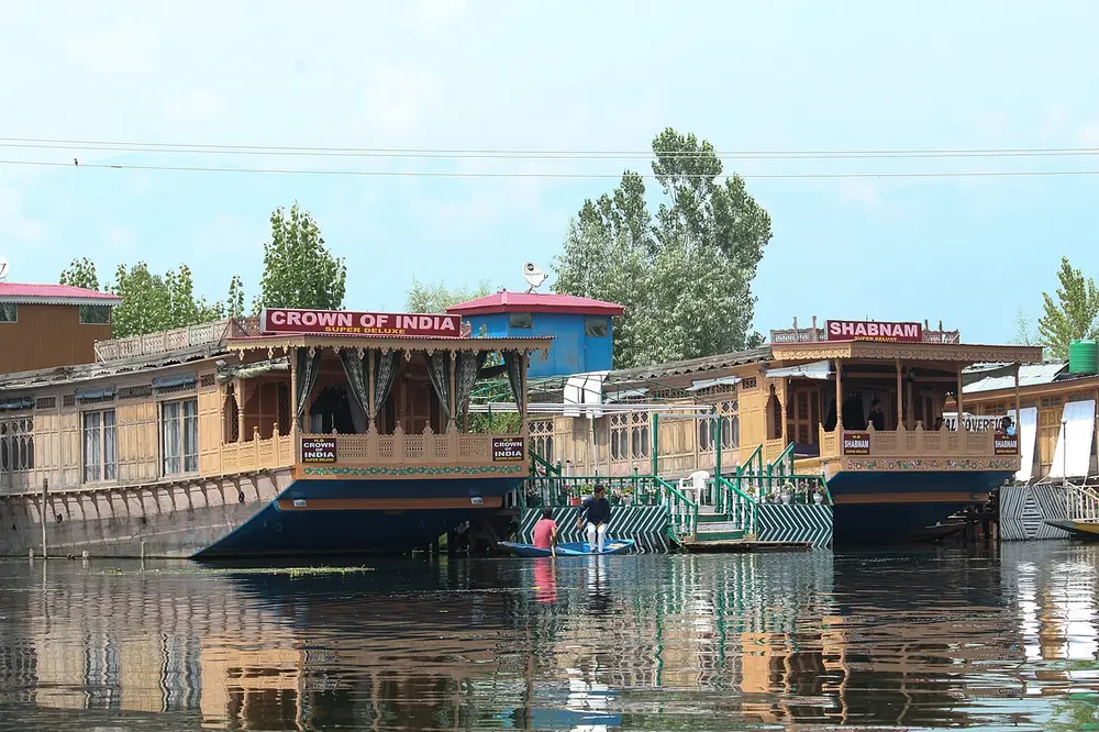 Carved wooden houseboats moored on a calm lake, with trees behind them.