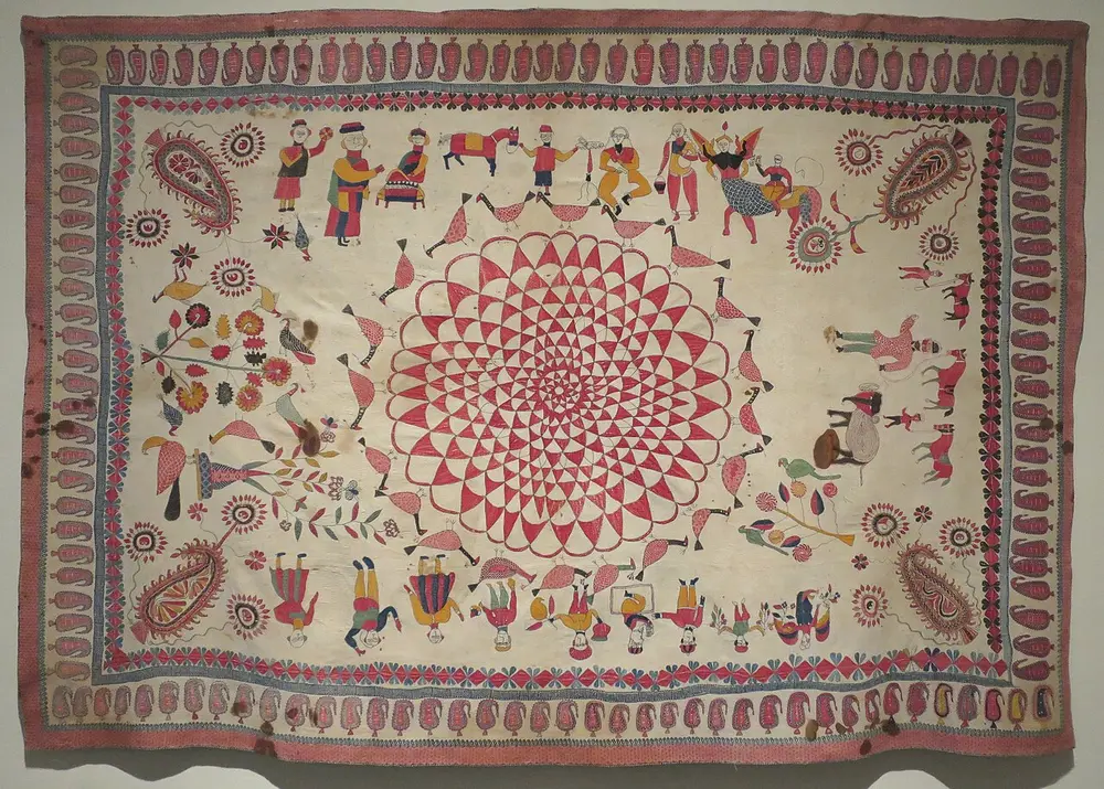 A white quilted bedcover embroidered with a big red lotus in the centre, surrounded by birds, horses, people and paisleys, with a paisley border.