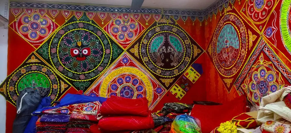 A shop wall in Pipli covered with bright appliqué hangings, made of cut red, yellow, green and black cloth, with the round-eyed face of Jagannath and peacocks.