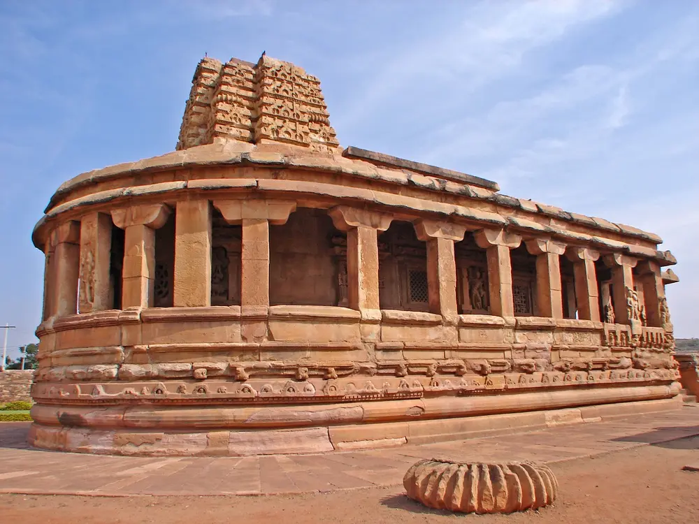 The Durga Temple at Aihole, a sandstone temple with a rounded back end, ringed by a pillared verandah, and a small square tower on the roof.