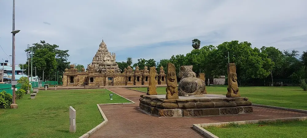 The Kailasanathar Temple at Kanchipuram, a low sandstone enclosure lined with small shrines, with a stepped pyramid tower rising behind, and a stone Nandi in the foreground.