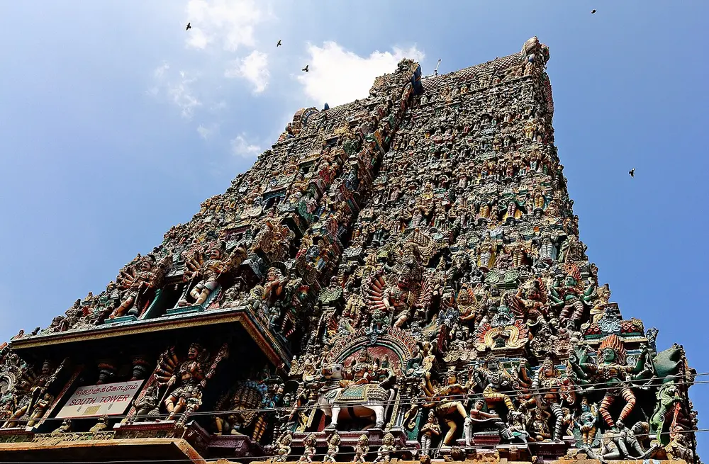 Looking up at the south gopuram of the Meenakshi Temple, a tall tapering tower covered from top to bottom with hundreds of brightly painted figures of gods and animals.