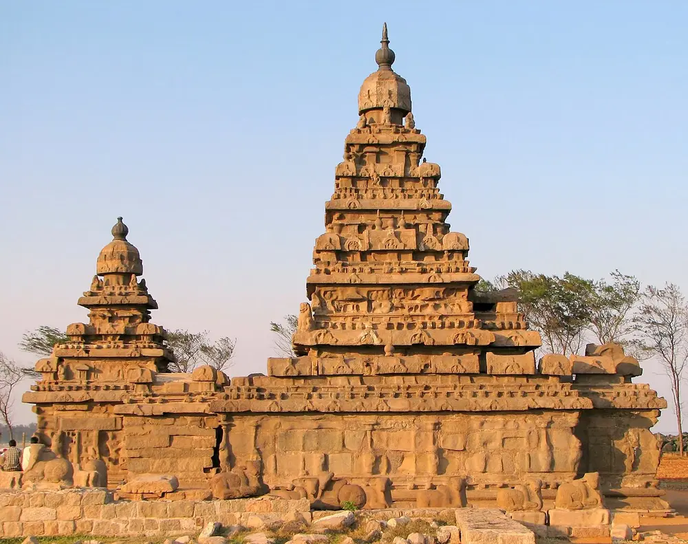 The Shore Temple, a weathered granite temple with two stepped pyramid towers, one tall and one small, under a clear sky.