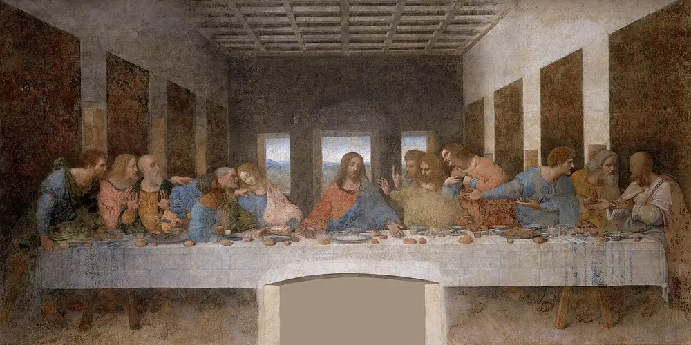 A long wall painting of Christ seated at the centre of a table with his twelve disciples in groups of three, reacting in alarm, in a room whose lines lead to a window behind him.