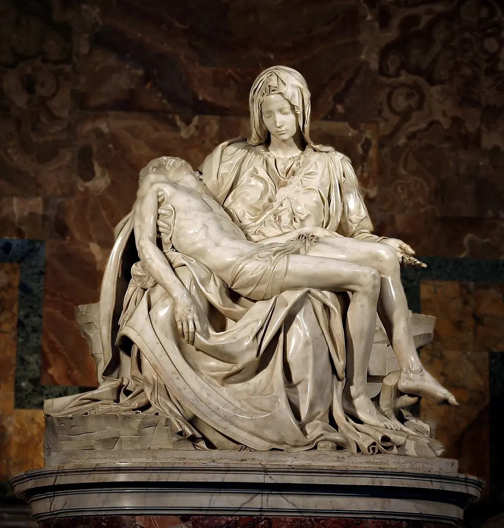 A white marble sculpture of a young-looking Mary seated, holding the body of the dead Christ across her lap, with deep folds in her robes.