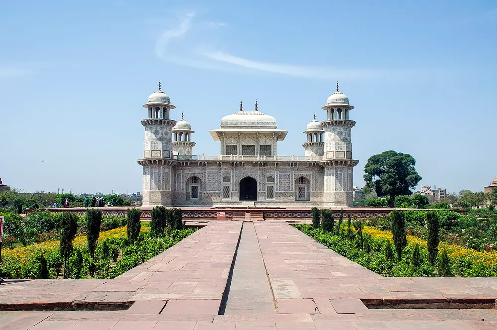 A square white marble tomb with an octagonal tower at each corner and a small canopied pavilion on its flat roof, at the end of a long garden path with a water channel.