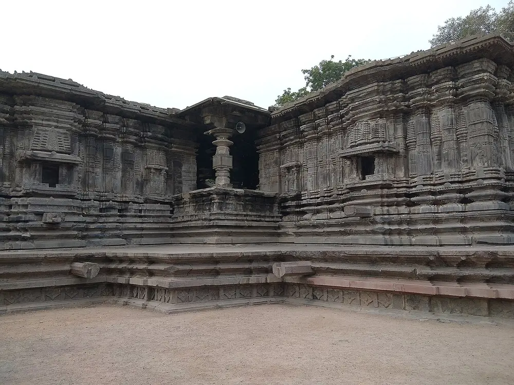 A low, dark grey stone temple with flat roofs and bands of fine carving, built in wings around an open stone platform.