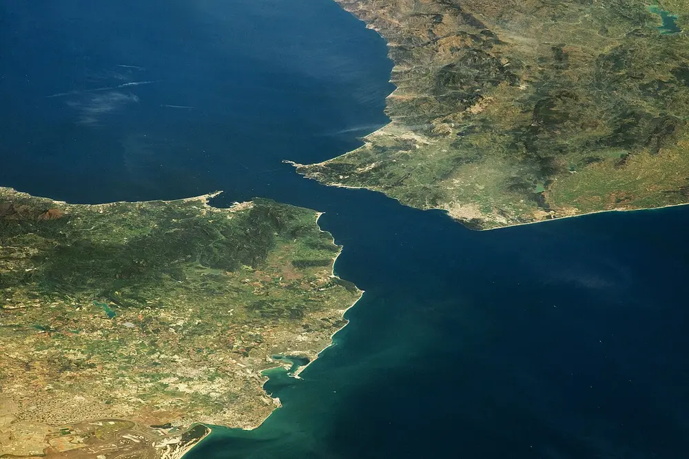 A photo from space of two green and brown coastlines almost touching across a narrow channel of dark blue sea.