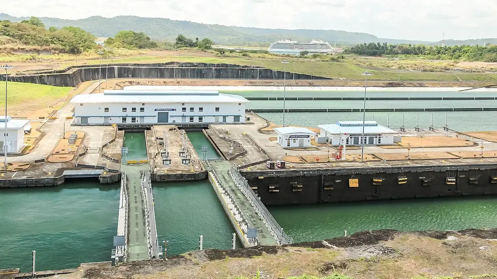 A set of huge concrete canal locks with water channels, gates and small control buildings, and a cruise ship in the distance.