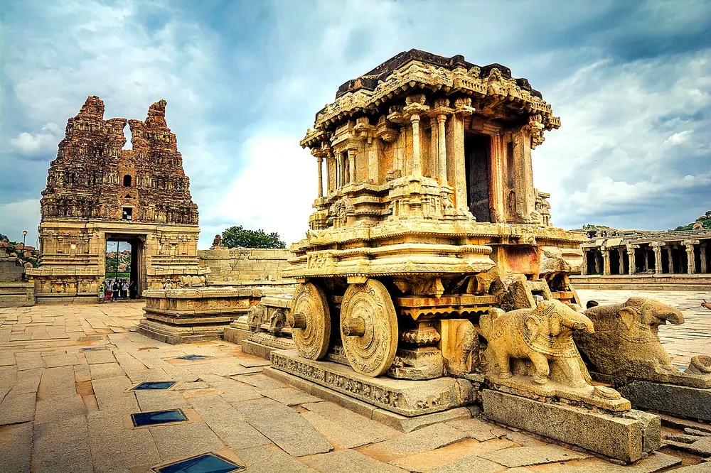 A carved stone shrine shaped like a chariot with stone wheels and stone elephants in front, in a temple courtyard.
