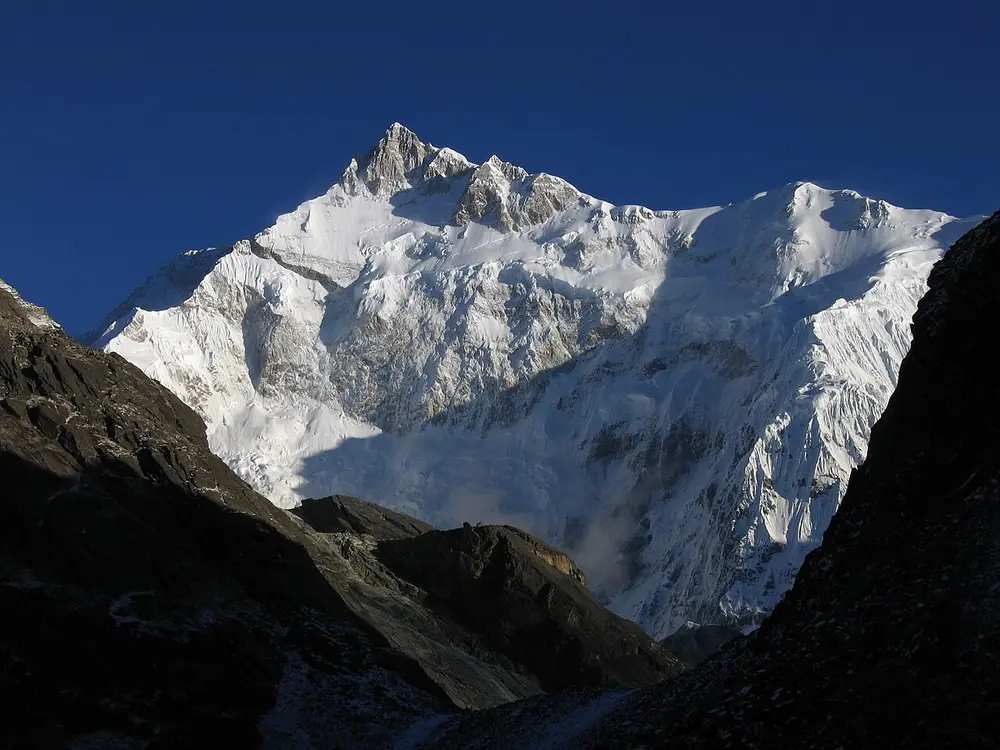 A huge snow-covered mountain face lit by sun, framed by dark rocky slopes.