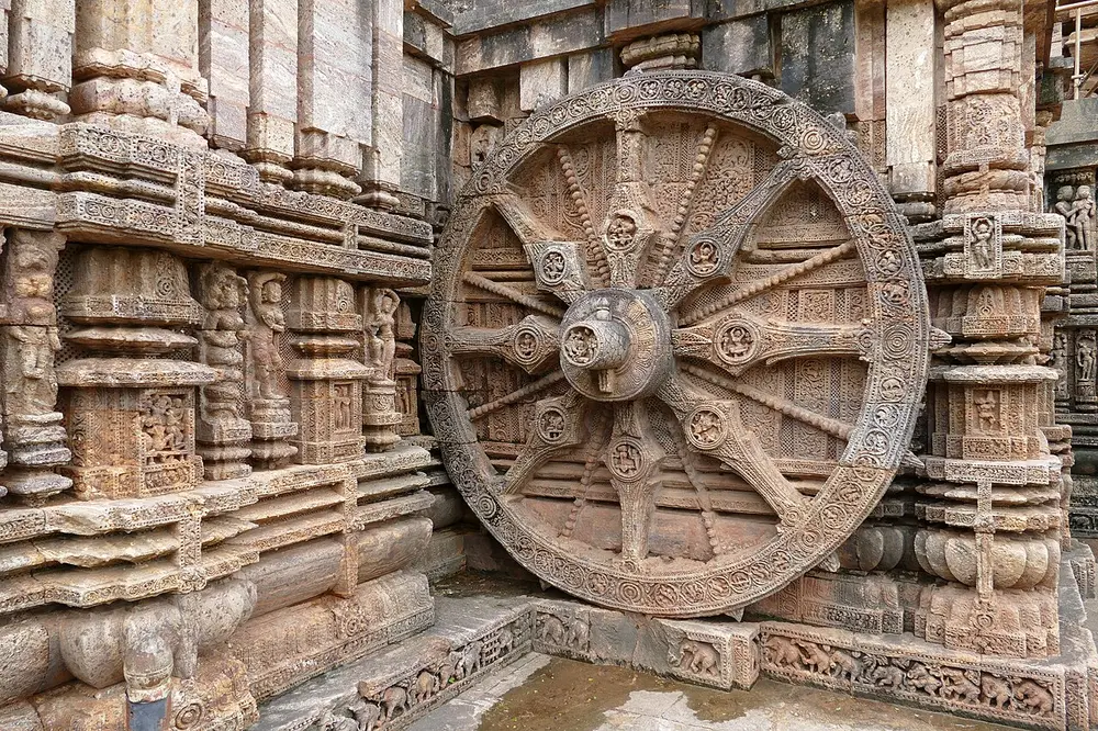 A giant carved stone wheel with spokes, set into the side of a temple wall covered in carvings.