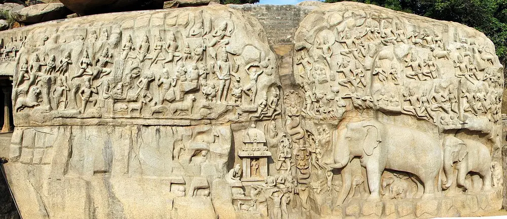 A long rock face carved with hundreds of gods, people and animals, with two life-size elephants on the right.