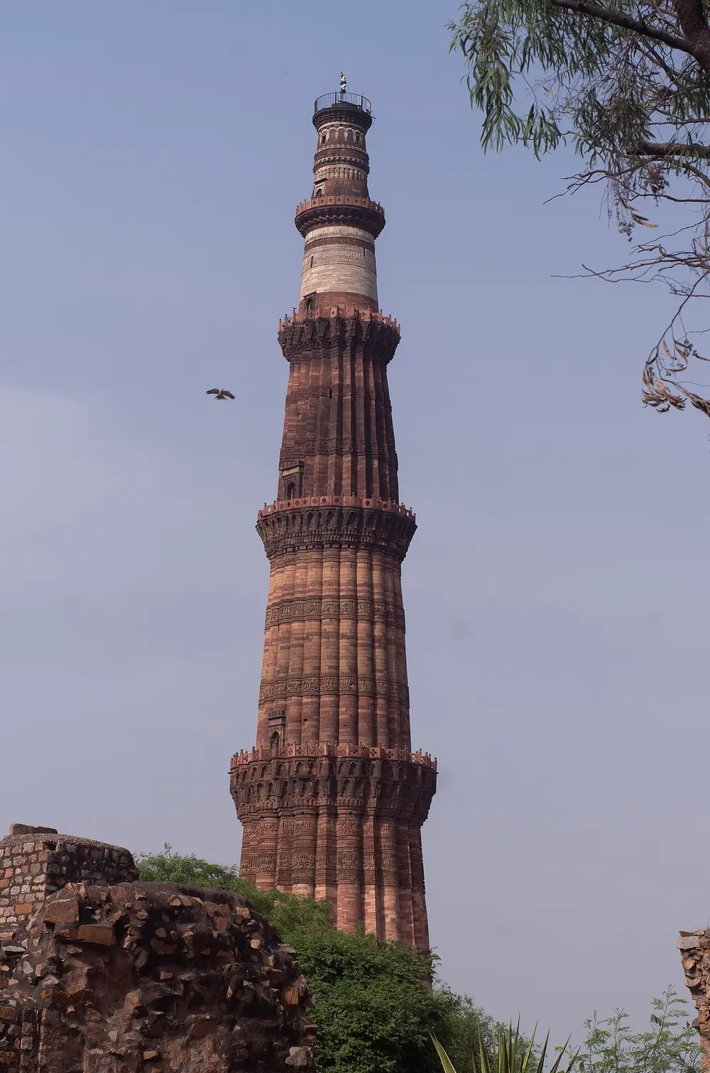 A very tall tapering tower of red and buff sandstone with balconies and bands of carved writing.