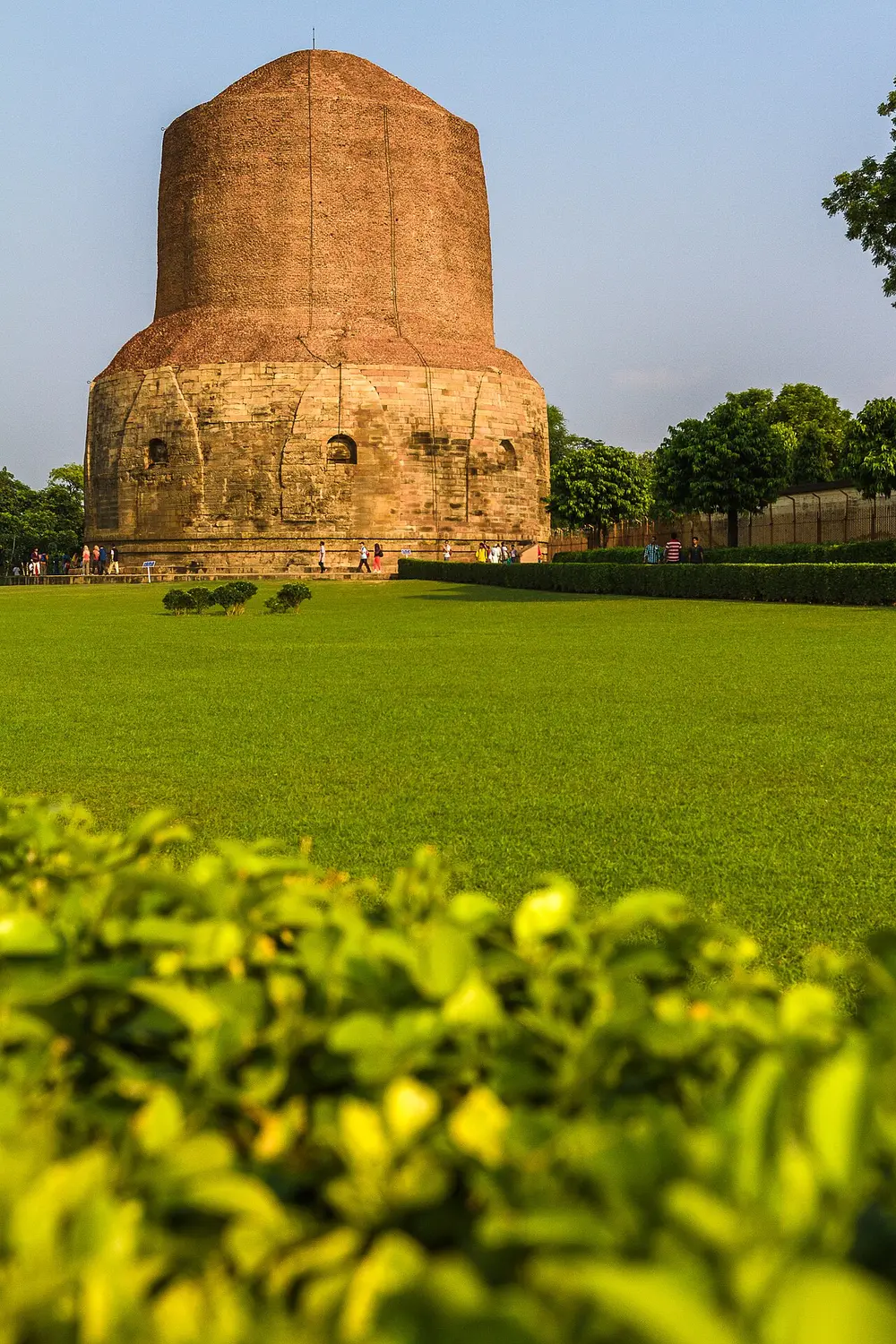 A massive round brick and stone stupa, like a short thick tower, standing in a wide green lawn.
