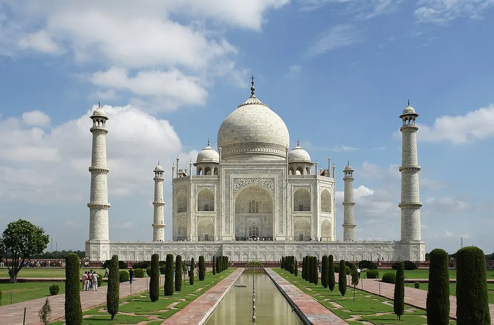The white marble Taj Mahal with its large dome and four minarets, seen across a long garden pool.