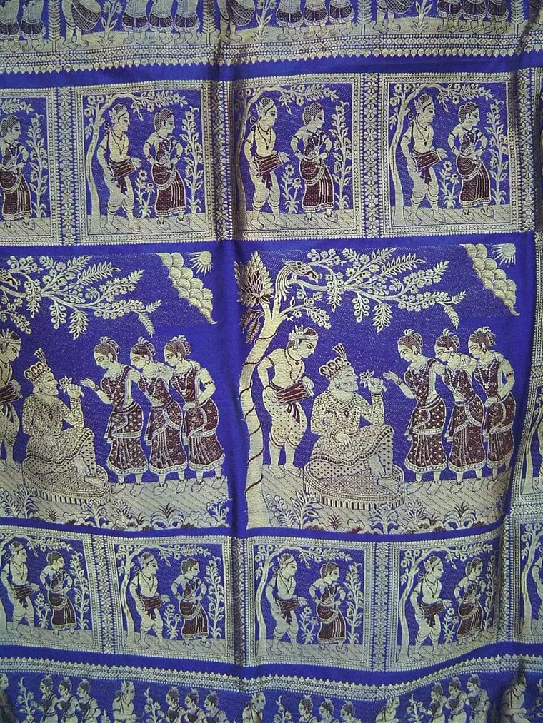 A blue silk sari pallu woven with panels of figures: a king seated under a tree with women around him, and rows of smaller figures in boxes.