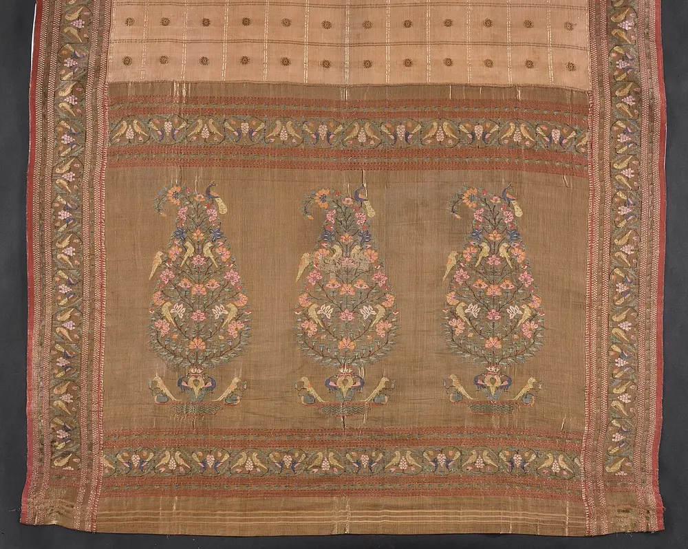 The end of an old silk sari showing three large tree-like motifs filled with flowers and birds, framed by borders of small parrots.